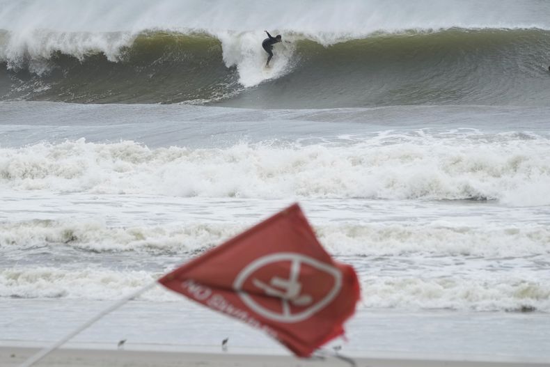 Una bandera que indica que está prohibido nadar en la playa mientras una persona surfea en Rockaway Beach, en Queens, Nueva York, el jueves 21 de agosto de 2025. (AP Foto/Seth Wenig)