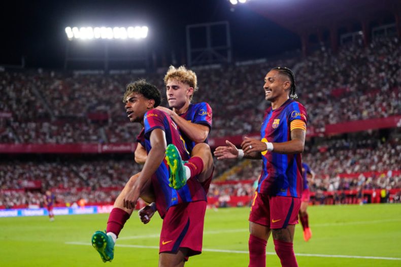 Raphinha (derecha), Lamine Yamal (izquiera) y Fermín López celebran el segundo gol del Barcelona en la victoria 3-1 ante Sevilla en la Liga española, el sábado 19 de septiembre de 2026, en Sevilla. (AP Foto/José Bretón)