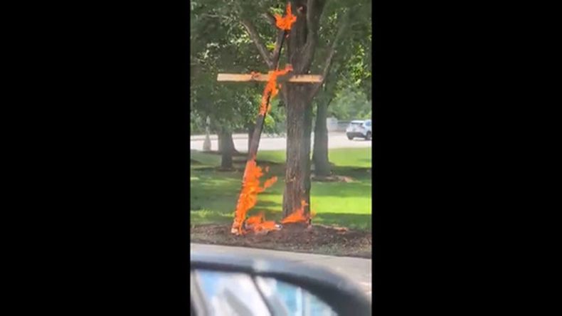 Esta escena de un video tomada por la conductora Keinika Carlton muestra una cruz de madera envuelta en llamas naranjas, apoyada sobre un árbol en Grant Park, Chicago, Illinois, el martes 9 de julio de 2026.(Keinika Carlton via AP)