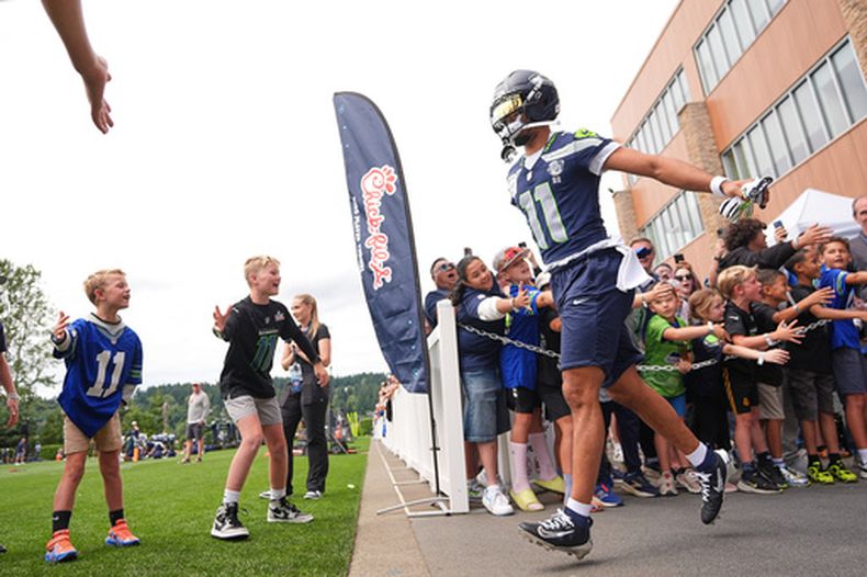 El receptor abierto de los Seahawks de Seattle, Jaxon Smith-Njigba, saluda a jóvenes aficionados mientras sale al campo durante el campamento de entrenamiento del equipo de la NFL, el domingo 26 de julio de 2026, en Renton, Washington. (Foto AP/Lindsey Wasson)