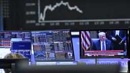 Tras una pantalla que muestra al presidente de Estados Unidos, Donald Trump, la pantalla con el índice bursátil Dax muestra un precio a la baja de las acciones en Fráncfort, Alemania, el jueves 3 de abril de 2025, después de Trump presentara un paquete de aranceles que llevó las bolsas a pérdidas. (Arne Dedert/dpa via AP)