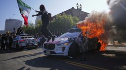 Un manifestante salta desde un taxi Waymo en llamas cerca del centro de detención metropolitano el domingo 8 de junio de 2025, en el centro de Los Ángeles. (AP Foto/Eric Thayer)