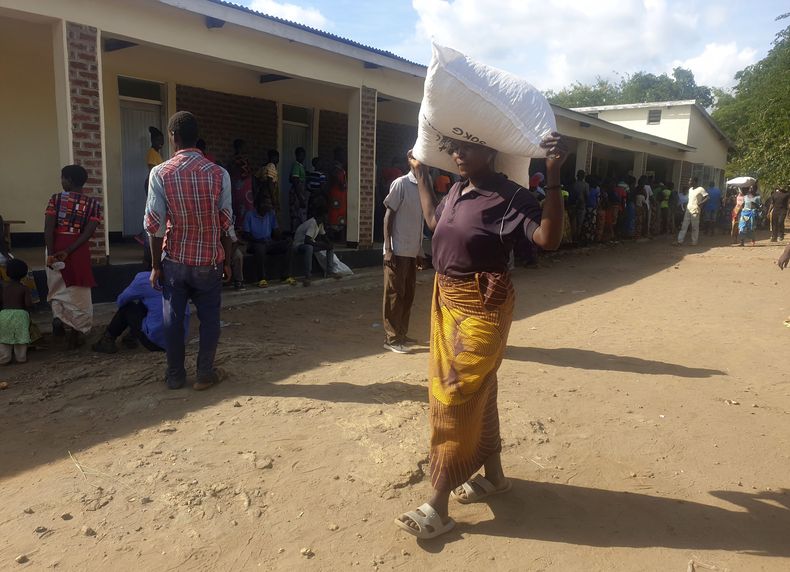Una mujer carga una bolsa de harina de maíz recibida en un centro de distribución del Programa Mundial de Alimentos en el distrito de Neno, en el sur de Malaui, el domingo 24 de marzo de de 2024. El presidente de Malaui, Lazarus Chakwera, ha declarado el estado de emergencia por la sequía en 23 de sus 28 distritos y afirmó que el país necesita urgentemente ayuda humanitaria por valor de 200 millones de dólares. (AP Foto/Kenneth Jali).