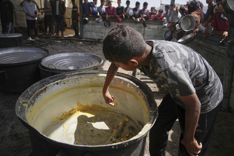 Un niño rebaña los restos de una olla vacía después de que se repartan las comidas en una cocina comunitaria en Jan Yunis, en el sur de la Franja de Gaza, el miércoles 4 de mayo de 2025. (AP Foto/Abdel Kareem Hana)