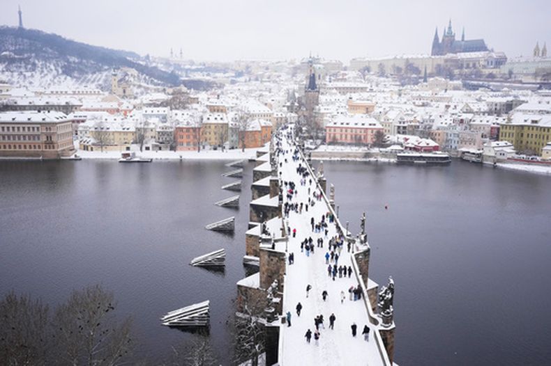 Varias personas cruzan el puente Carlos tras una fuerte nevada en Praga, República Checa, el viernes 9 de enero de 2026. (AP Foto/Petr David Josek)