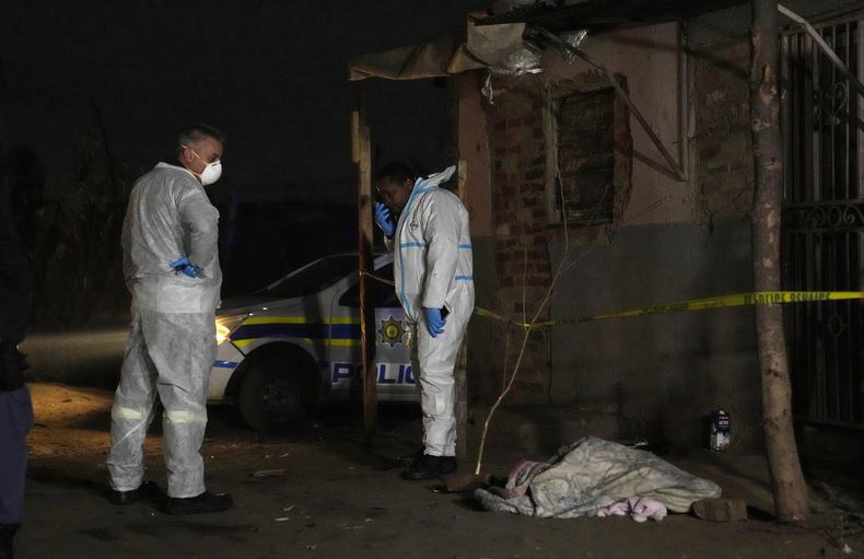 Dos policías permanecen cerca de un cadáver en el asentamiento Angelo el jueves 6 de julio de 2023, en Boksburg, Sudáfrica. Una fuga de gas dejó más de una decena de muertos en el asentamiento. (AP Foto/Themba Hadebe)