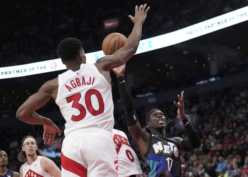 Dennis Schroder (17), de los Nets de Brooklyn, ataca la canasta con la marca defensiva de Ochai Agbaji (30), de los Raptors de Toronto, durante la segunda mitad del juego de baloncesto de la NBA, el lunes 25 de marzo de 2024, en Toronto. (Nathan Denette/The Canadian Press vía AP)