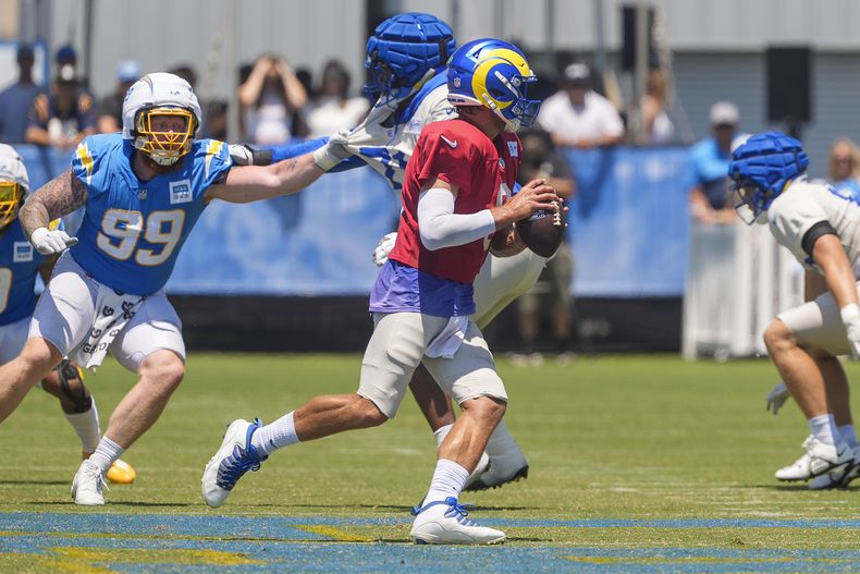 Matthew Stafford, de rojo, quarterback de los Rams de Los Ángeles, corre con el balón durente una práctica conjunta ante los Chargers de Los Ángeles, en The Bolt, en El Segundo, California, el domingo 4 de agosto de 2024. El tackle defensivo de los Chargers Scott Matlock (99) busca presionar a Stafford. (AP Foto/Damian Dovarganes)