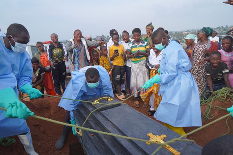Personas vestidas con trajes protectores colocan en una tumba un féretro que contiene los restos de Jeannine Katusabe, quien falleció de ébola, durante un servicio funerario, el martes 11 de agosto de 2026, en Bunia, en la provincia de Ituri, en República Democrática del Congo. (AP Foto/Dieudonne Dirole)