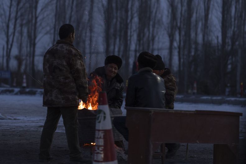 Hombres reunidos en torno a una hoguera en un control de carretera para entrar en el condado Wushi en la región occidental china de Xinjiang, el martes 23 de enero de 2024. Un enorme sismo remeció una zona poco poblada de la región occidental china de Xinjiang, donde causó unas pocas muertes y dañó o derribó más de 120 viviendas en pleno invierno. (AP Foto/Ng Han Guan)