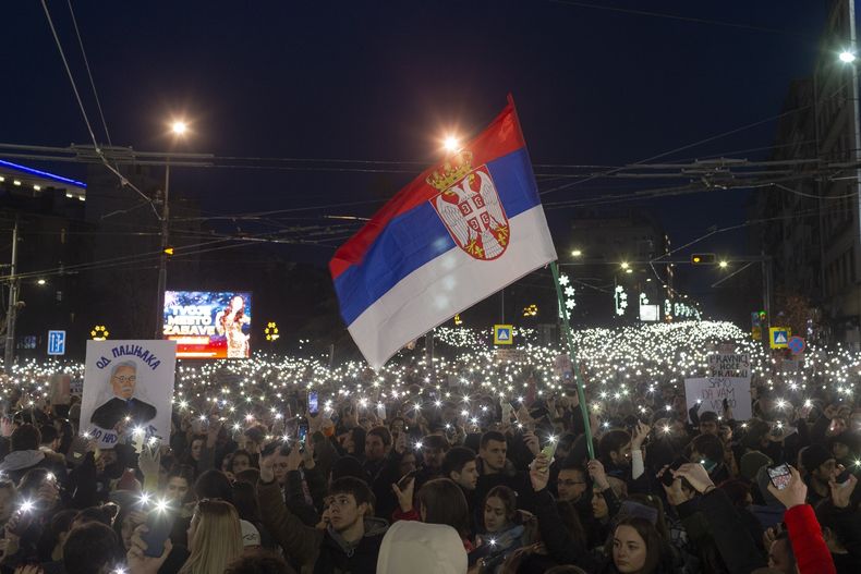 ARCHIVO - Una bandera serbia ondea al viento, mientras varias personas usan las linternas de sus teléfonos móviles en una protesta contra el presidente populista Aleksandar Vucic y su gobierno, cuyo férreo control del poder se ha visto desafiado por semanas de protestas callejeras lideradas por estudiantes universitarios, en Belgrado, Serbia, el lunes 22 de diciembre de 2024. (AP Foto/Marko Drobnjakovic, Archivo)