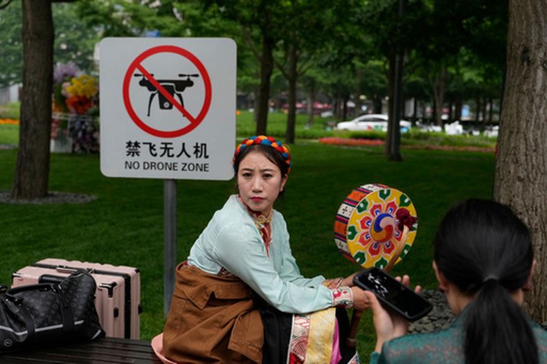 Una intérprete descansa junto a un cartel que prohíbe los drones en Beijing, el 31 de mayo de 2023 (AP Foto/Ng Han Guan)