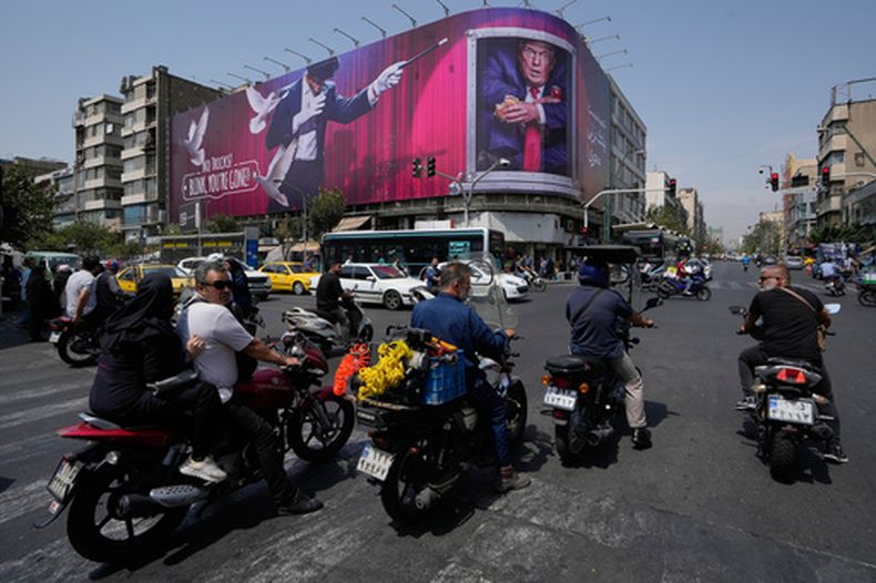 Vehículos pasan junto a una valla publicitaria que muestra al presidente estadounidense Donald Trump junto a un mago y las palabras ¡No trucos! ¡Parpadea, te has ido, en el centro de Teherán, Irán, lunes 31 de agosto de 2026. (Foto AP/Vahid Salemi)