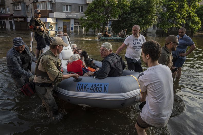 Soldados ucranianos llegan en un bote cargados con civiles tras sacarlos de una zona inundada en la localidad de Kardashynka, en la orilla izquierda del río Dniéper, en Jersón, Ucrania, el 9 de junio de 2023. Muchas embarcaciones pequeñas, con rescatistas y soldados a bordo, cruzan desde zonas controladas por Ucrania en la orilla oeste para rescatar a civiles desesperados varados en tejados, áticos y otras zonas altas. (AP Foto/Evgeniy Maloletka)