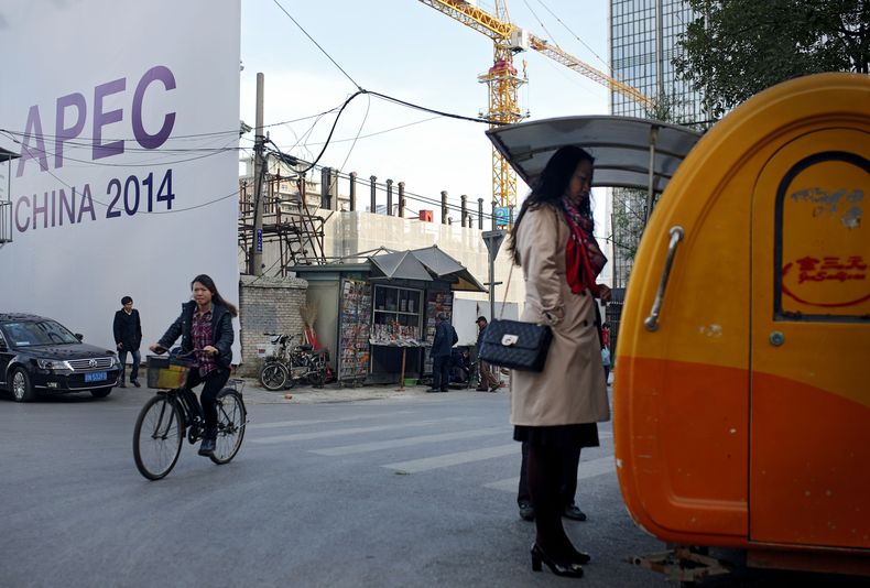 En esta imagen, tomada el 6 de noviembre de 2014, una mujer (a la derecha) compra su desayuno en un puesto callejero mientras un hombre ojea un diario en un quiosco de prensa cerca de un anuncio sobre la cumbre APEC, en Beijing, China. (Foto AP/Andy Wong)