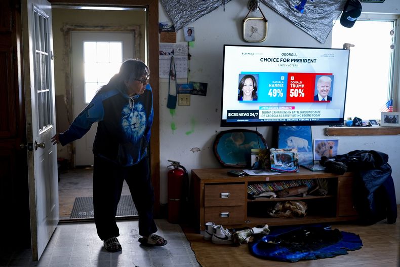 Alice Aishanna entra en su salón mientras una emisión de CBS News muestra a la candidata presidencial demócrata Kamala Harris y al candidato presidencial republicano, el expresidente Donald Trump, el martes 15 de octubre de 2024, en su casa de Kaktovik, Alaska. (AP Foto/Lindsey Wasson)