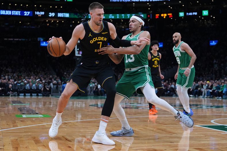 El pívot de los Warriors de Golden State Kristaps Porzingis avanza hacia la canasta frente al base de los Celtics de Boston Ron Harper Jr. el miércoles 18 de marzo del 2026. (AP Foto/Charles Krupa)