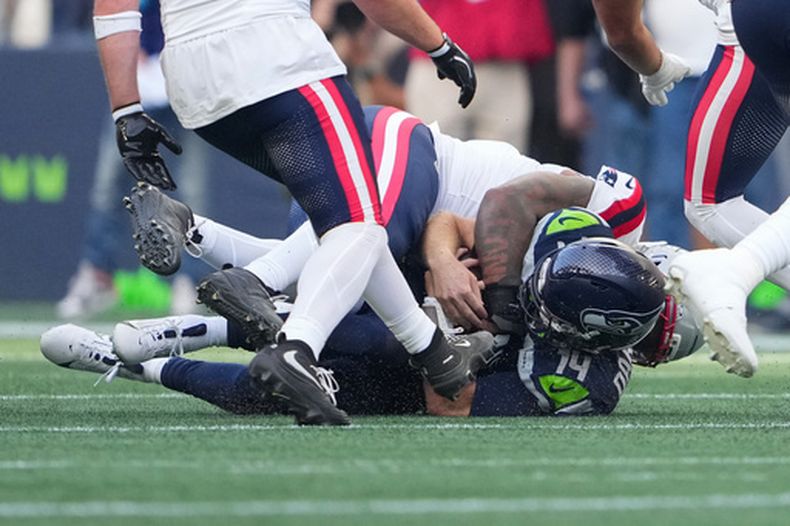El quarterback de los Seahawks de Seattle, Sam Darnold (14), es capturado por el linebacker de los Patriotas de Nueva Inglaterra, Dremont Jones (al fondo), durante la primera mitad de un partido de fútbol americano de la NFL, el miércoles 9 de septiembre de 2026, en Seattle. (Foto AP/Lindsey Wasson)
