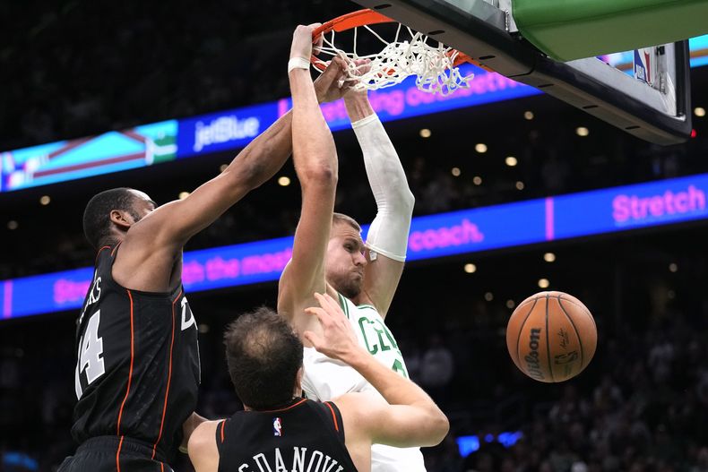 El lituano Kristaps Porzingis, pívot de los Celtics de Boston, realiza una clavada frente a Alec Burks (izquierda) y Bojan Bogdanovic, de los Pistons de Detroit, en la prórroga del partido del jueves 28 de diciembre de 2023 (AP Foto/Charles Krupa)