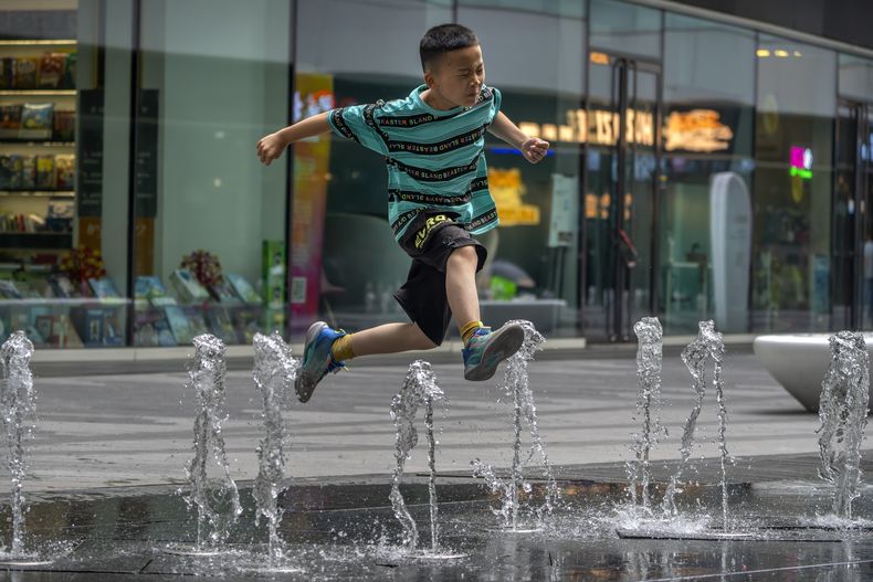 Un niño salta sobre una fuente en un complejo comercial y de oficinas en Beijing, el sábado 1 de julio de 2023. El sábado se emitió una alerta naranja, el segundo más alto, en la capital China cuando las temperaturas volvieron a rondar los 40 grados Celsius (104 Fahrenheit) en una prolongada ola de calor. (AP Foto/Mark Schiefelbein)