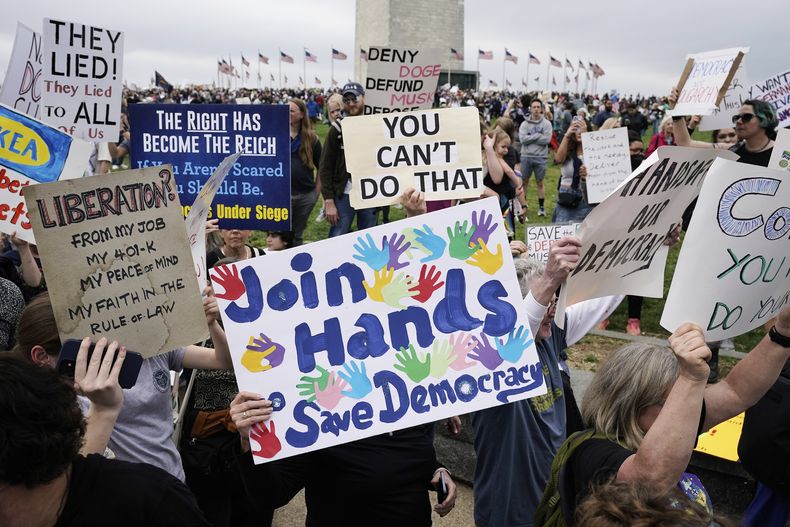 Manifestantes sostienen carteles durante una protesta de ¡Manos fuera! contra el presidente Donald Trump en el Monumento a Washington en Washington, el sábado 5 de abril de 2025. (AP foto/Jose Luis Magana)