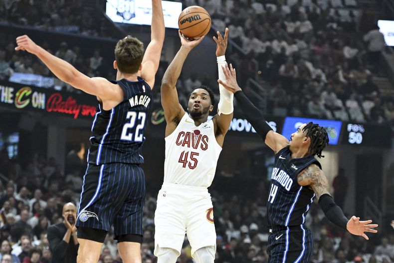 Donovan Mitchell de los Cavaliers de Cleveland lanzó un intento de tres frente a Franz Wagner y Gary Harris del Magic de Orlando en el juego 1 de la serie de primera ronda de la postemporada el sábado 20 de abril del 2024. (AP Foto/Nick Cammett)