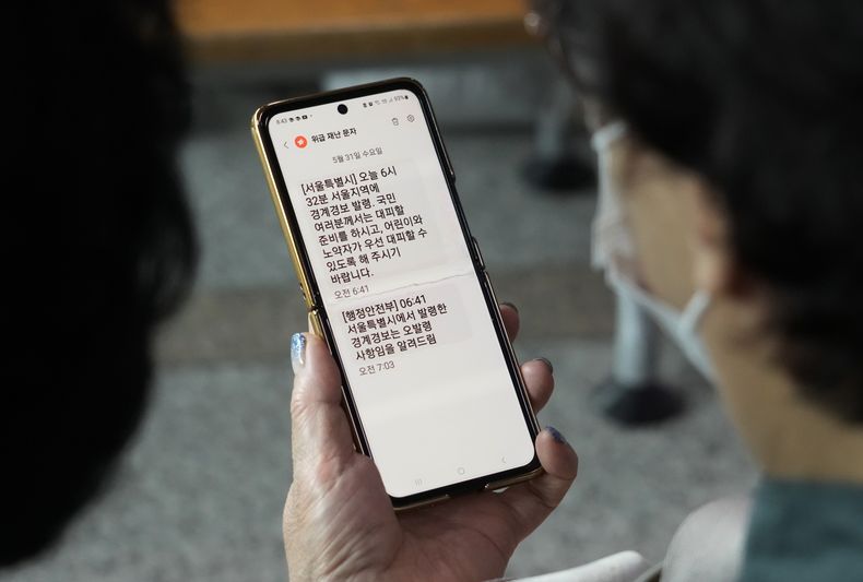 Una mujer lee en su teléfono celular un aviso de evacuación de emergencia enviado a habitantes de Seúl mientras mira un noticiero en la TV en Seúl, Corea del Sur, miércoles 31 de mayo de 2023. El aviso provocó miedo en la población aunque el lanzamiento de un satélite espía por Corea del Norte fracasó. (AP Foto/Ahn Young-joon)