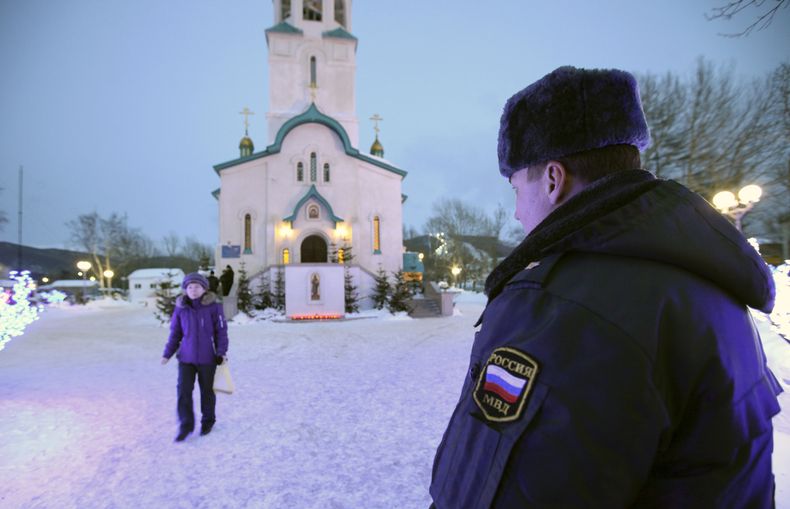 Un polic&iacute;a vigila mientras una persona se retira de la Catedral de la Resurrecci&oacute;n de Cristo en la ciudad rusa de Yuzhno-Sajalinsk, en la isla de Sajalin, el domingo 9 de febrero de 2014, donde un individuo armado con un fusil mato a dos per