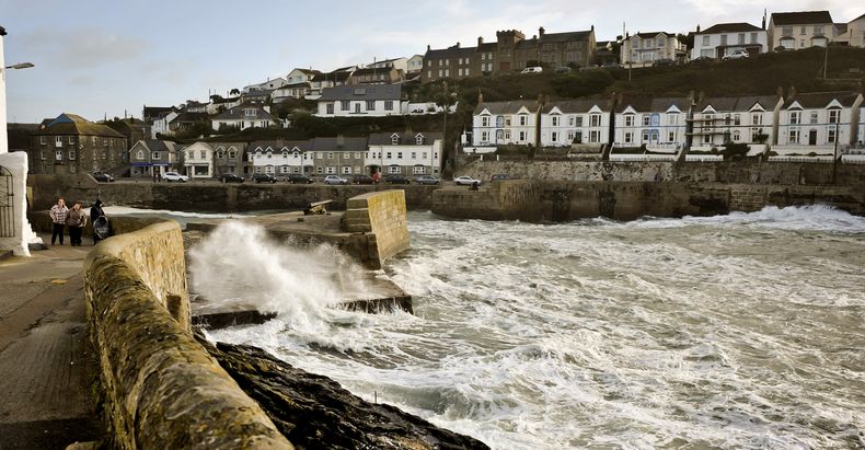 La gente camina mientras las olas se estrellan conra el malec&oacute;n que protege la bah&iacute;a de Porthleven, Cornwall, en el domingo 27 de octubre de 2013. (Foto AP/PA, Ben Birchall)