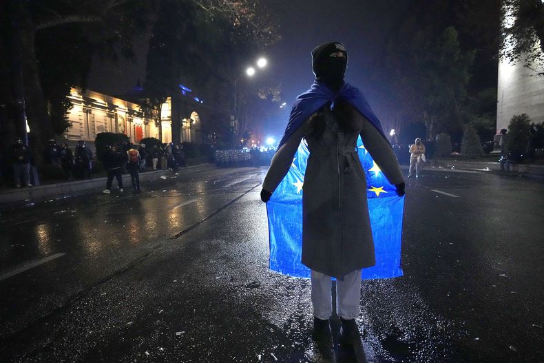 Una mujer sostiene una bandera de la Unión Europea en una protesta contra la decisión del gobierno de suspender las negociaciones para unirse al bloque, en Tiflis, Georgia, la madrugada del sábado 7 de diciembre de 2024. (AP Foto/Pavel Bednyakov)