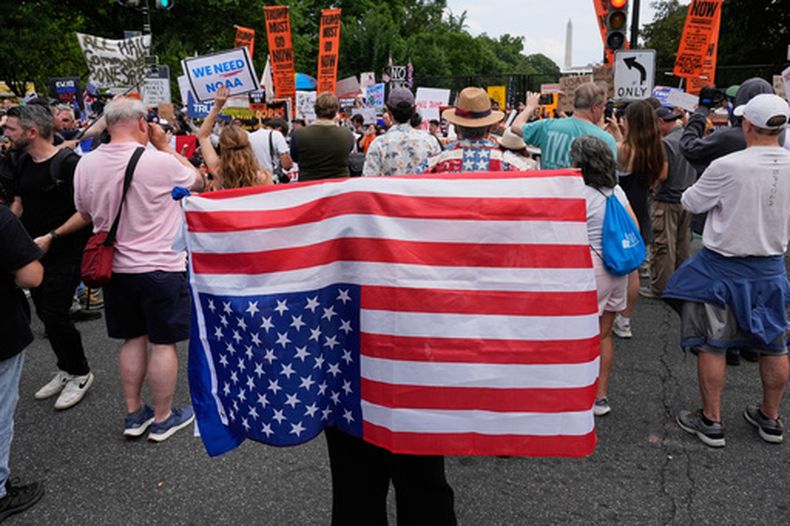 ARCHIVO - Una persona lleva una bandera estadounidense del revés durante una protesta cerca de la Casa Blanca en el día de un desfile militar para conmemorar el 250 aniversario del Ejército de Estados Unidos, y que coincidía con el 79 cumpleaños del presidente, Donald Trump, el 14 de junio de 2025 en Washington. (AP Foto/Alex Brandon, Archivo)