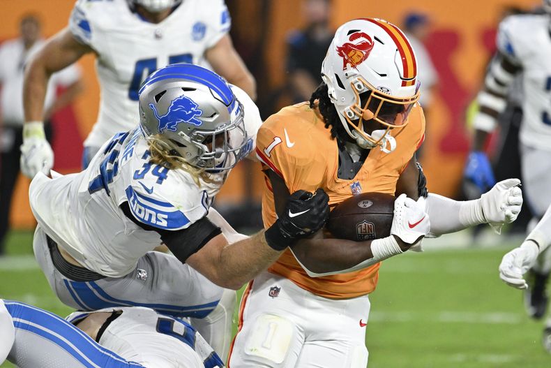 Rachaad White (1), corredor de los Buccaneers de Tampa Bay, es derribado por el linebacker de los Lions de Detroit, Alex Anzalone (34), durante la segunda mitad del juego de la NFL, el domingo 15 de octubre de 2023, en Tampa, Florida. (AP Foto/Jason Behnken)