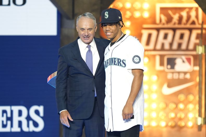 El comisionado del Béisbol de Grandes Ligas, Rob Manfred, izquierda, y Jurrangelo Cijntje, posan después de que Cijntje fuera seleccionado en el puesto 15 por los Marineros de Seattle en la primera ronda del draft de béisbol de la MLB en Fort Worth, Texas, el domingo 14 de julio de 2024. (Foto AP/ LM Otero)