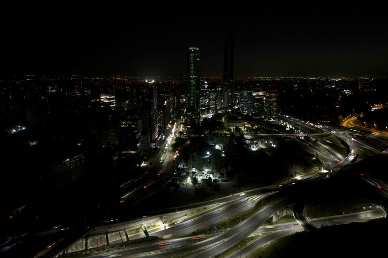 Los automóviles pasan velozmente entre edificios oscuros durante un corte de energía en Santiago, Chile, el martes 25 de febrero de 2025. (AP Foto/Matías Basualdo)