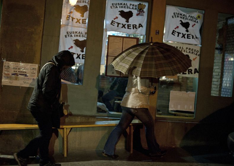 Dos personas pasan junto a un bar en el que hay carteles que piden que todos los miembros de la proscrita organizaci&oacute;n vasca ETA regresen a las c&aacute;rceles, en Tafalla, Navarra, el mi&eacute;rcoles 23 de octubre del 2013. Miles de personas se r