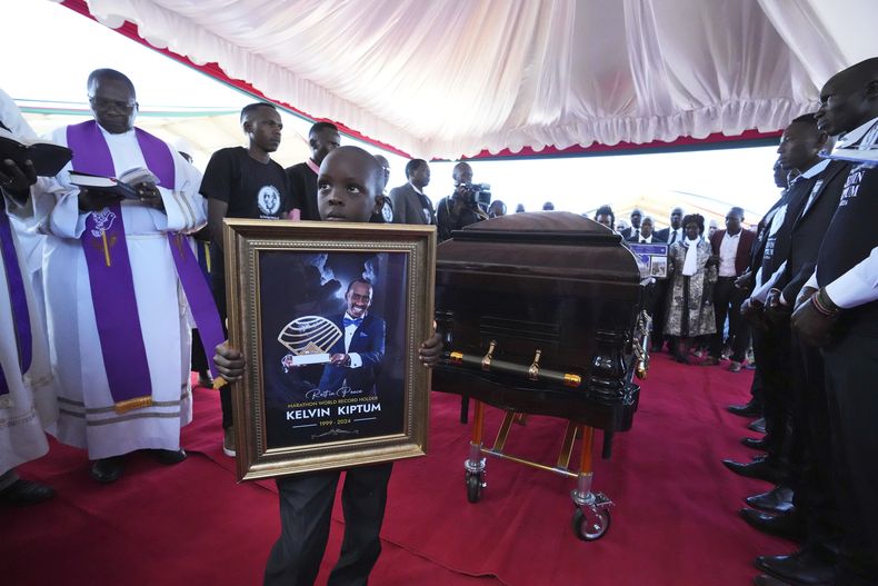 Caleb Kigen, hijo del maratonista Kelvin Kiptum sostiene una foto de su padre durante el entierro del maratonista que estableció un nuevo récord del mundo en Elgeyo Marakwet, Kenia el viernes 23 de febrero del 2024. (AP Foto/Brian Inganga)