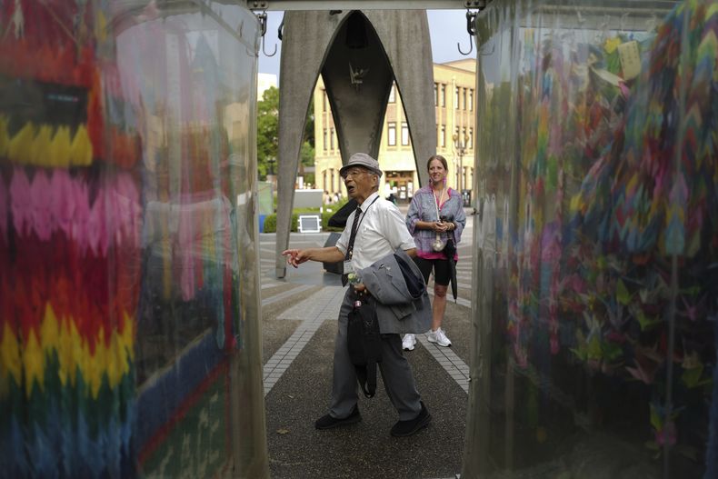 Kunihio Iida, sobreviviente de la bomba atómica y guía voluntario habla en inglés a visitantes extranjeros frente al Monumento a la Paz de los Niños, donde la gente deposita grullas de papel en honor a las víctimas de la bomba atómica de 1945, el 9 de julio de 2025, en Hiroshima, Japón. (AP Foto/Eugene Hoshiko)