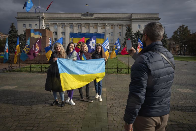 Residentes sostienen una bandera ucraniana mientras posan para una fotografía mientras la ciudad de Jersón celebra el primer aniversario desde que recuperó el control de la ciudad de manos de las fuerzas rusas, en la plaza central de Jersón, Ucrania, el sábado 11 de noviembre de 2023. (AP Foto/Efrem Lukatsky)