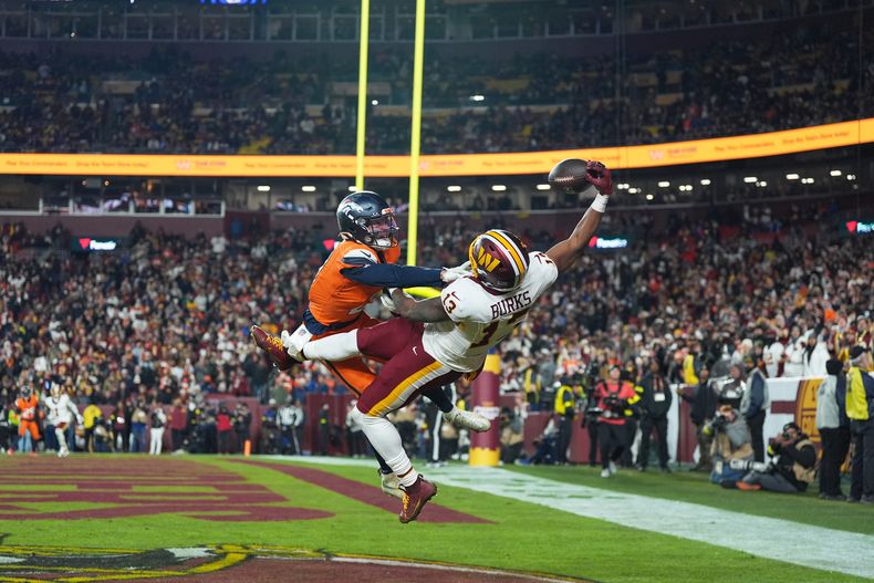 El wide receiver Treylon Burks (13), de los Commanders de Washington, atrapa un pase de touchdown con una mano mientras Riley Moss, izquierda, de los Broncos de Denver, defiende durante la segunda mitad del partido de la NFL, el domingo 30 de noviembre de 2025, en Landover, Maryland. (AP Foto/Stephanie Scarbrough)
