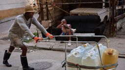 Un hombre empuja un carrito lleno de bidones de agua mientras otro descansa en un sofá en una calle de La Habana, Cuba, el jueves 27 de agosto de 2026. (Foto AP/Ramón Espinosa)