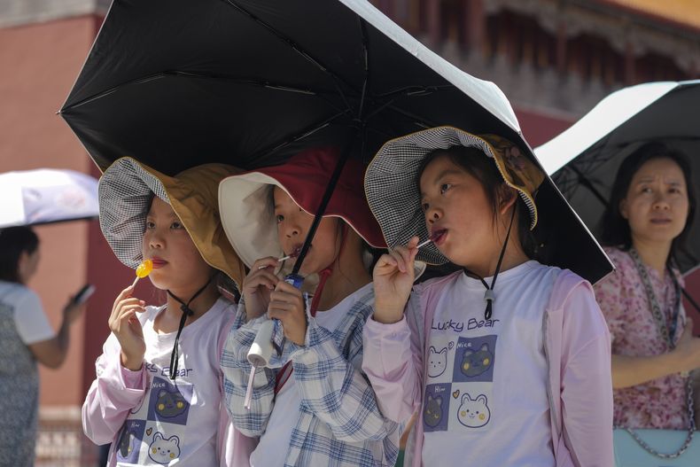 Niños con gorras para sol y paraguas posan para una foto cerca de la Ciudad Prohibida en una jornada de calor sofocante en Beijing, viernes 7 de julio de 2023. (AP Foto/Andy Wong)