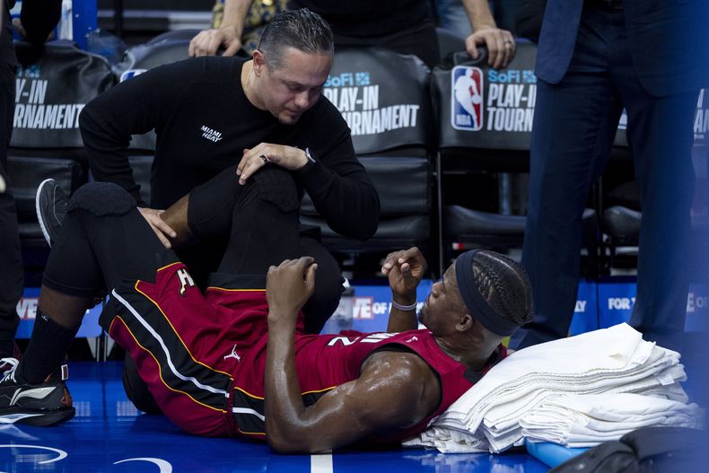Jimmy Butler, del Heat de Miami, a la derecha, recibe tratamiento en su rodilla derecha por parte del personal de entrenamiento durante la primera mitad del partido del torneo de play-in de baloncesto de la NBA del equipo contra los 76ers de Filadelfia, el miércoles 17 de abril de 2024, en Filadelfia. Los 76ers ganaron 105-104. (AP Foto/Chris Szagola)