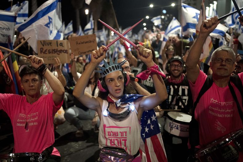 Una manifestante porta una corona como la de Estatua de la Libertad y una bandera estadounidense durante una protesta contra los planes del primer ministro israelí Benjamin Netanyahu para reformar el sistema judicial de la nación, frente a la oficina de la embajada de Estados Unidos en Tel Aviv, el jueves 13 de julio de 2023. (AP Foto/Maya Alleruzzo)