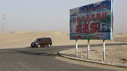 ARCHIVO - Un auto maneja por un desierto donde un cartel dice Bienvenido al Nuevo Pueblo Unidad Hotan, en Hotan, en la región occidental china de Xinjiang, el 21 de septiembre de 2018. (AP Foto/Andy Wong, Archivo)