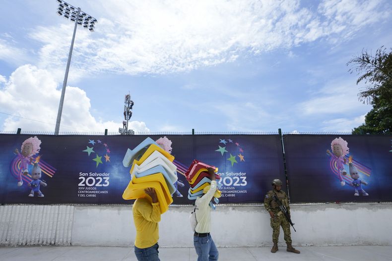 Dos trabajadores cargan butacas a ser instaladas en el Estadio Mágico González de San Salvador, el jueves 22 de junio de 2023, a un día de la inauguración de los Juegos Centroamericanos y del Caribe (AP Foto/Arnulfo Franco)