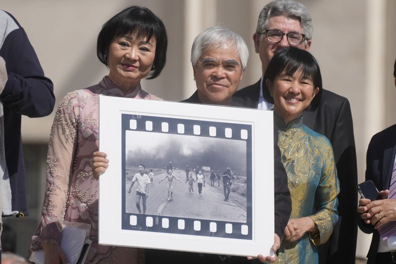 ARCHVO - El fotógrafo ganador del Premio Pulitzer, Nick Ut, en el centro, flanqueado por Kim Phuc, a la izquierda, sostiene a la Chica del Napalm, su fotografía ganadora del Premio Pulitzer en la que Phuc aparece huyendo desnuda, mientras esperan reunirse con el Papa Francisco durante la audiencia general semanal en la Plaza de San Pedro en The Vaticano, miércoles 11 de mayo de 2022. (Foto AP/Gregorio Borgia, archivo)