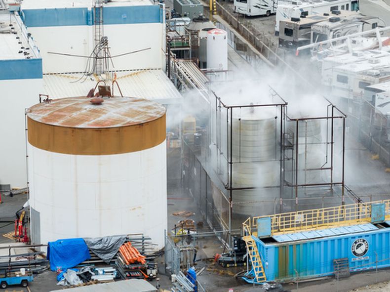 Un tanque dañado es rociado con agua en GKN Aerospace en Garden Grove, Caliornia, el domingo 24 de mayo después de que el tanque, que contiene un producto químico para fabricar piezas de plástico, se sobrecalentara el jueves. (AP Foto/Ethan Swope)