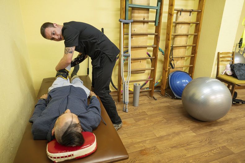 El doctor Alexis Cholas, izquierda, examina la pierna amputada de un soldado ucraniano en el centro de rehabilitación de un hospital en Kiev, 8 de noviembre de 2023. La pérdida de su brazo derecho puso fin a su carrera de cirujano. Pero sigue yendo al frente como parte de un grupo de médicos voluntarios llamados Hospitallers y trabaja en el hospital como especialista en rehabilitación. (AP Foto/Evgeniy Maloletka)