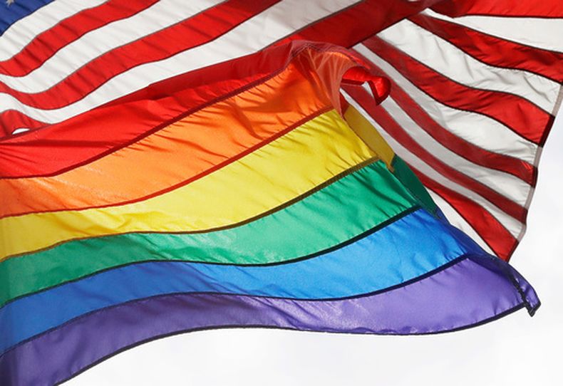 ARCHIVO - Una bandera LGBTQ+ ondea tras una bandera estadounidense en el monumento nacional de Stonewall en Nueva York, el 11 de octubre de 2017. (AP Foto/Mark Lennihan, Archivo)