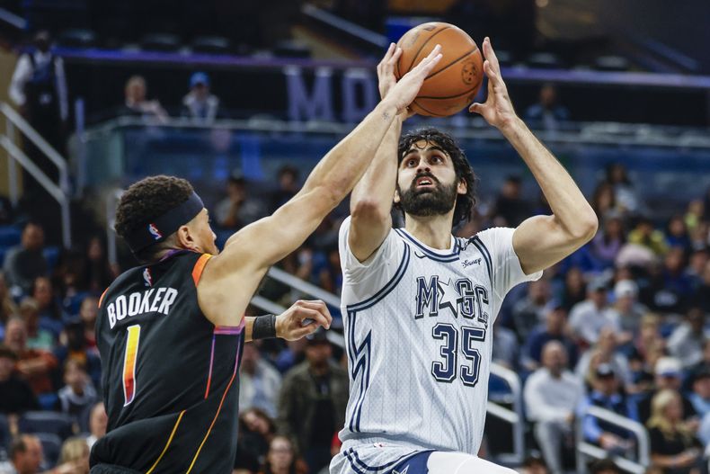 Devin Booker (1), de los Suns de Phoenix, defiende un tiro de Goga Bitadze (35), del Magic de Orlando, durante la primera mitad del juego de baloncesto de la NBA, el domingo 8 de diciembre de 2024, en Orlando, Florida. (AP Foto/Kevin Kolczynski)